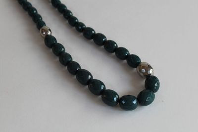 necklace made of green glass beads with silver accents on a white surface