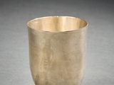 silver cup sitting on a table with a shadow on the ground
