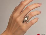 woman ' s hand holding a ring with a pearl in it