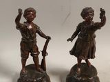 pair of bronze figurines of a boy and a girl with a gun