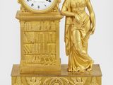 a gold clock with a woman standing next to it