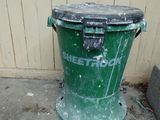 a green trash can sitting on the sidewalk next to a building