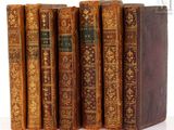 six old books are lined up in a row on a white surface