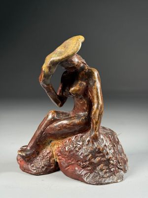 bronze sculpture of a woman sitting on a rock with a hat on her head