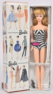 une poupée Barbie dans une boîte, avec des vêtements et des accessoires posés dessus