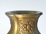 a gold vase sitting on a table with a white wall in the background