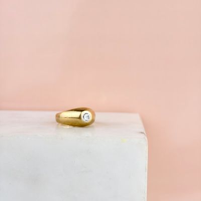 une bague en or sertie d'un diamant repose sur un bloc de marbre