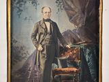 an old picture of a man in a suit standing next to a chair