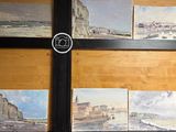 de nombreux tableaux accrochés au mur d'une pièce où se trouve une horloge