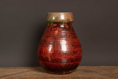 un vase rouge posé sur une table en bois, sur fond noir