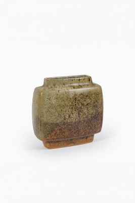 un vase vert au pied marron posé sur une surface blanche