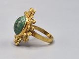 an image of a gold ring with a green stone surrounded by leaves