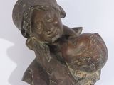 statue en bronze représentant une femme tenant un enfant dans ses bras, posée sur une surface blanche