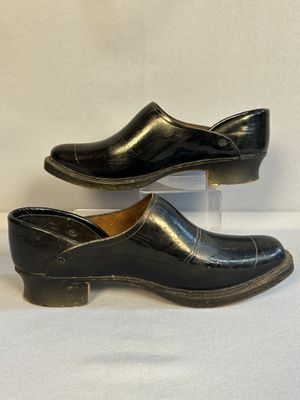 une paire de sabots en cuir noir exposés sur une surface blanche