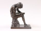 bronze statue of a man sitting on a rock with his hands on his knees