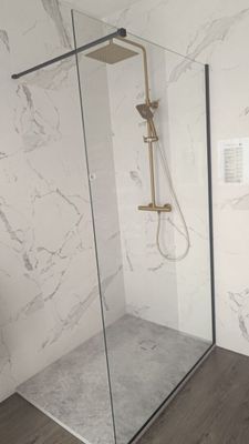 une douche avec une porte vitrée, à côté des toilettes