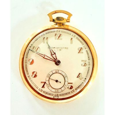 gros plan d'une montre de poche en or sur une surface blanche