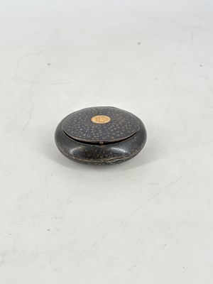 une image représentant une boîte noire et dorée posée sur une surface blanche