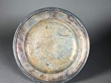 an antique silver plate sitting on top of a gray surface