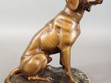 bronze statue of a dog sitting on a rock on a gray surface