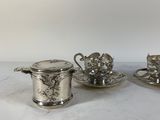 three silver plated tea cups and saucers on a white surface