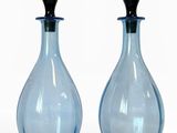 deux bouteilles en verre bleues avec des bouchons noirs, posées sur une surface blanche