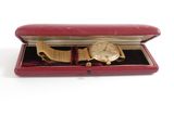 a gold watch in a red case on a white surface