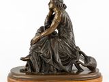a bronze statue of a woman sitting on top of a wooden base