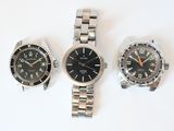 three watches are sitting on a white surface, one is black and the other is silver