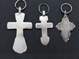 three silver cross charms on a black background