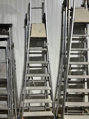 Plusieurs échelles sont alignées contre un mur dans un entrepôt.