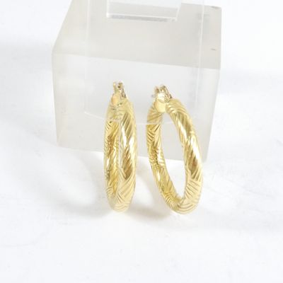 une paire de boucles d'oreilles créoles dorées présentées dans un présentoir en acrylique transparent