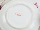 a white plate with a pink flower on it and a cup and saucer