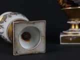 a white and gold vase sitting next to a gold and white vase