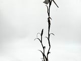 statue représentant un oiseau en plein vol au-dessus d'une plante, sur fond blanc