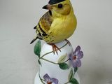 a small yellow bird sitting on top of a white vase