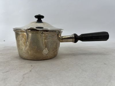 une vieille saucière en argent avec une poignée noire, posée sur une table