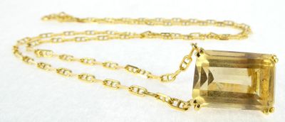 a close up of a necklace on a white surface with a gold chain