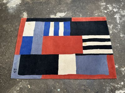 an image of a rug on the ground with a red, black, blue, and white design