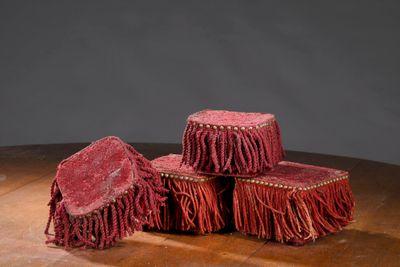 trois tabourets rouges à franges posés sur une table en bois