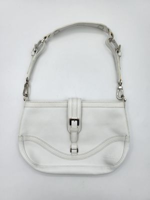 un sac à main blanc posé sur une surface blanche, muni d'une poignée en métal