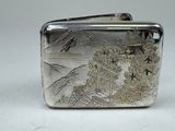 a silver cigarette case with a mountain scene on it