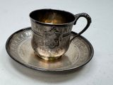 a silver cup and saucer sitting on a white table