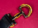 black leather dog leash with a gold buckle on a pink background