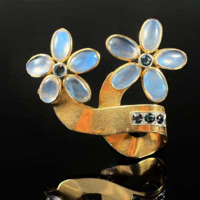 an image of a gold and blue flower broochle on a black surface