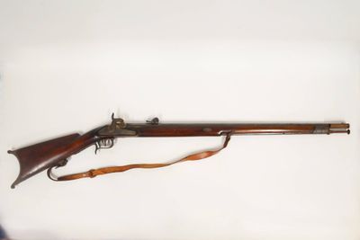 Un vieux fusil est posé sur une surface blanche, tandis qu'un homme l'observe