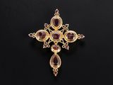 a gold and garnet stone cross pendant on a black background