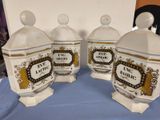 three white and gold canisters with labels on them on a blue table