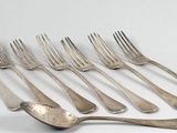 six forks and a spoon are lined up on a white surface