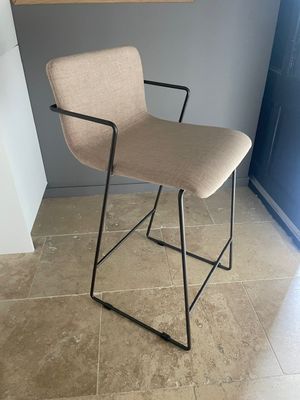 une chaise beige aux pieds et accoudoirs noirs, placée devant une porte bleue